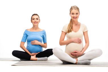 two beautiful pregnant women sitting on floor and smiling isolated on white clipart