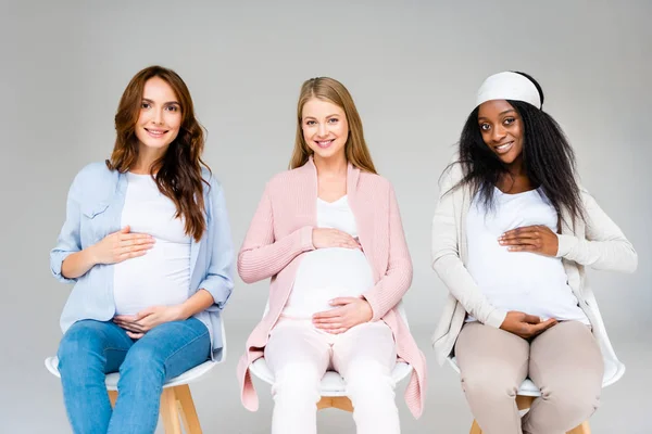 Mujeres Embarazadas Multiétnicas Sentadas Sillas Tocando Vientres Aisladas Gris —  Fotos de Stock
