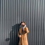 Handsome businessman in coat talking on smartphone and holding coffee to go