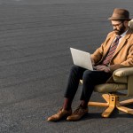 Adult bearded businessman sitting in armchair and using laptop