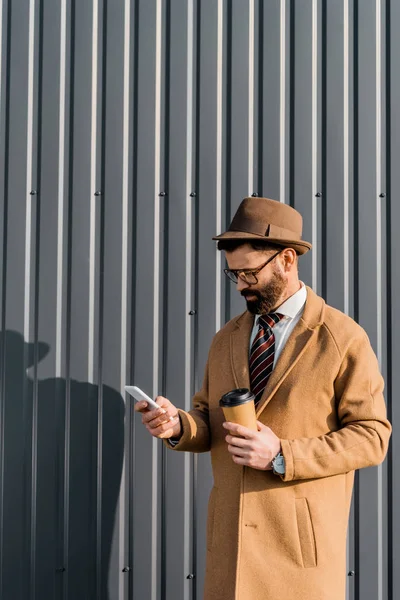 商人在外套和眼镜使用智能手机和举行咖啡去 — 免费的图库照片