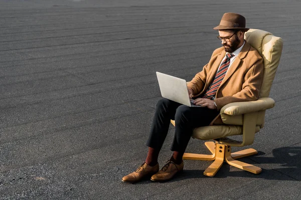 大人髭実業家肘掛け椅子に座っているとラップトップを使用して  — 無料ストックフォト