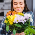 Krásná šťastná dívka se zavřenýma očima drží kytici květin doma