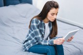 high angle view of young woman sitting on bed and using digital tablet