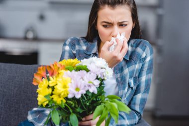 girl with allergy holding facial tissue and looking at flowers  clipart