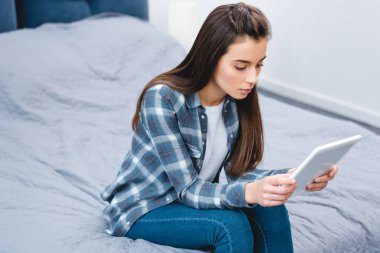 Yatağın üstüne oturan ve dijital tablet kullanarak genç kadının yüksek açılı görünüş