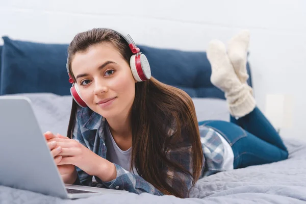 Όμορφη Νεαρή Γυναίκα Στα Ακουστικά Χρησιμοποιώντας Laptop Στο Κρεβάτι Και — Φωτογραφία Αρχείου