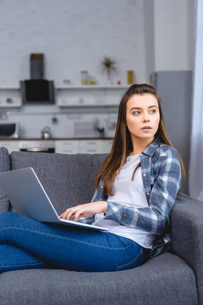 young woman using laptop on couch and looking away at home