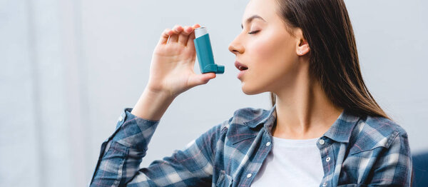 girl using inhaler while suffering from asthma at home 