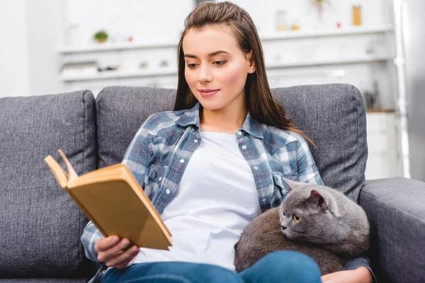 Leende Ung Kvinna Läsa Bok Och Sitter Med Katten Soffan — Stockfoto