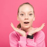 Surprised blonde kid looking at camera, isolated on pink