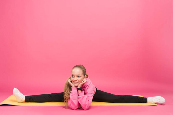 adorable youngster doing split on fitness mat, isolated on pink