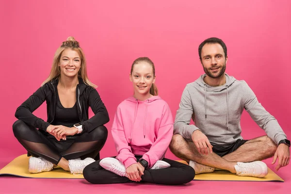 sportive family sitting on fitness mat, isolated on pink