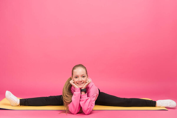 happy female child doing split on fitness mat, isolated on pink