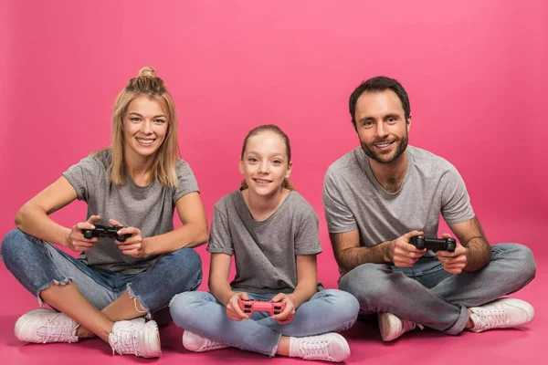 beautiful family playing video game with joysticks, isolated on pink