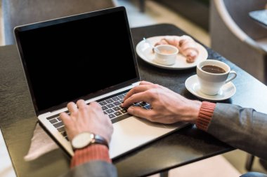restoranda boş ekran ile Laptop yazarken kahve ve kruvasan ile masada oturan işadamı kırpılmış görünümü