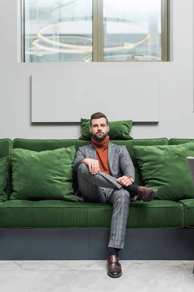 Mann Formell Drakt Med Beina Krysset Sittende Grønn Sofa Kamera – stockfoto