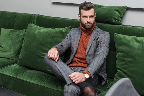 Mann Formeller Kleidung Mit Überkreuzten Beinen Sitzt Auf Grünem Sofa — kostenloses Stockfoto