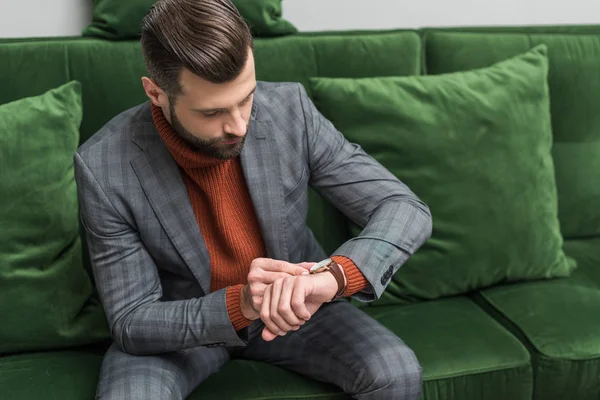 Człowiek Wizytowym Siedząc Kanapie Zielony Regulacja Zegarek Strony — Darmowe zdjęcie stockowe