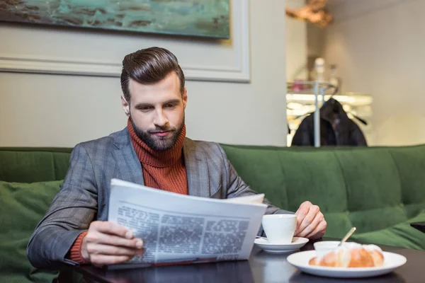 stylish man in formal wear sitting at table with coffee and reading newspaper in restaurant
