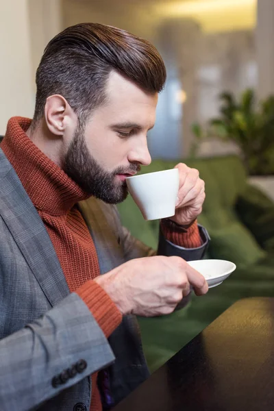 handsome bearded man in formal wear drinking coffee in restaurant