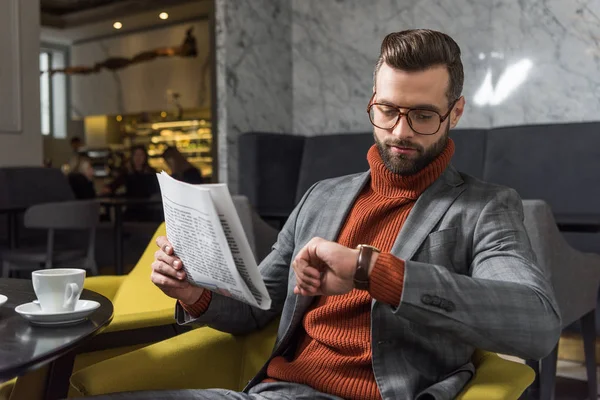 Stylowy Mężczyzna Wizytowym Okulary Trzymając Gazetę Patrząc Zegarek Restauracji — Darmowe zdjęcie stockowe