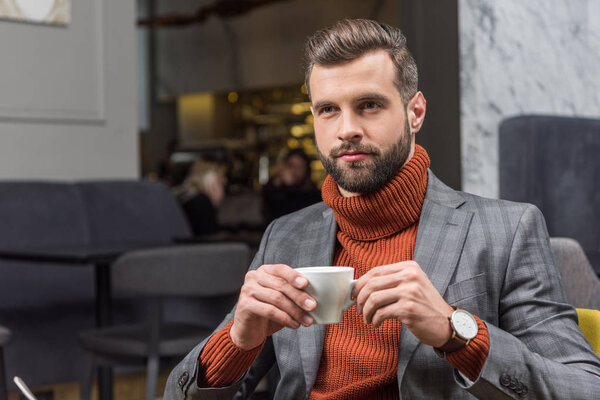 handsome bearded man in formal wear drinking coffee in restaurant