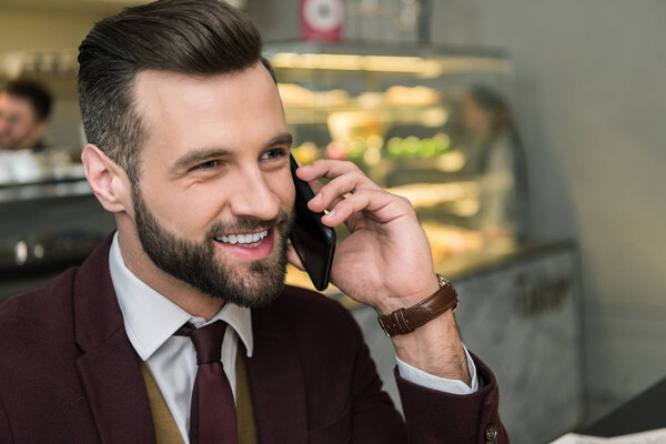 handsome smiling businessman in formal wear talking on smartphone