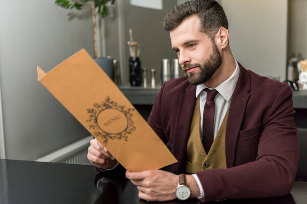 красивый бизнесмен в формальной одежде сидит в ресторане и держит меню
 