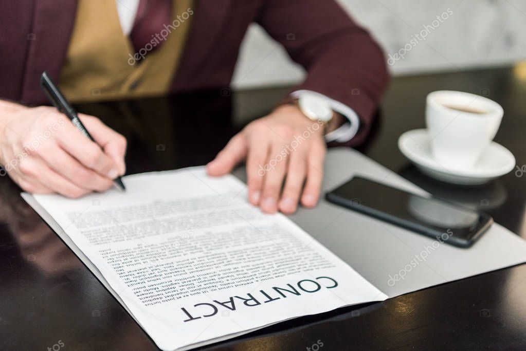 cropped view of businessman in formal wear sitting at table and signing contract 