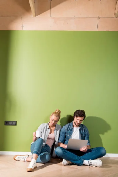 Attractive Girl Sitting Floor Holding Coffee Cup Husband Typing Laptop — Free Stock Photo