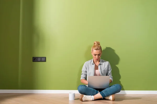 Atrakcyjna Dziewczyna Wpisując Klawiaturze Laptopa Siedzi Podłodze Przez Zielony Ściana — Zdjęcie stockowe