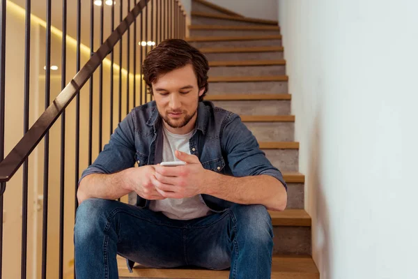 Όμορφος Άνδρας Κάθεται Σκαλοπάτια Και Χρησιμοποιώντας Smartphone Στο Σπίτι — Φωτογραφία Αρχείου