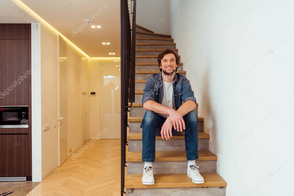 cheerful man smiling and sitting on stairs at home