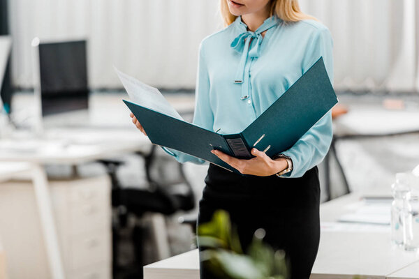 partial view of businesswoman with folder in office
