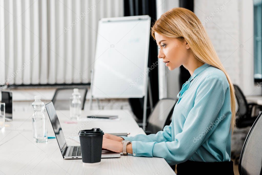 side view of focused businesswoman working on laptop in office
