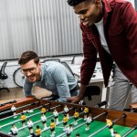 Sorridentes empresários multiculturais jogando futebol de mesa no escritório