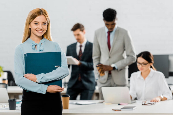 selective focus of businesswoman with folder and multiethnic colleagues in office