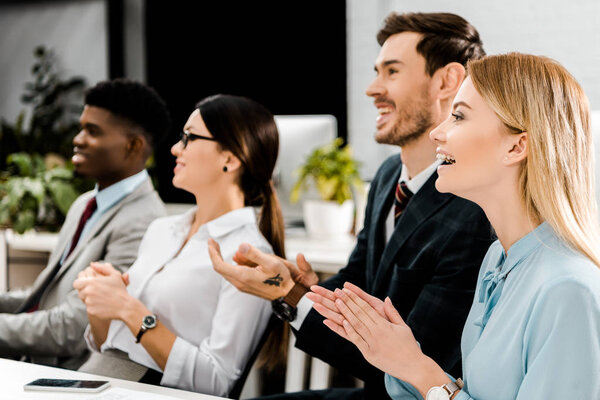 улыбающиеся мультирасовые бизнесмены аплодируют спикеру в офисе
