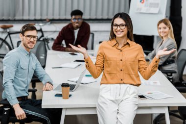 gülümseyen iş kadını ofiste çok ırklı meslektaşları ile kameraya bakıyor