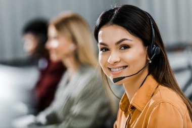 selective focus of smiling female call center operator in headset in office clipart