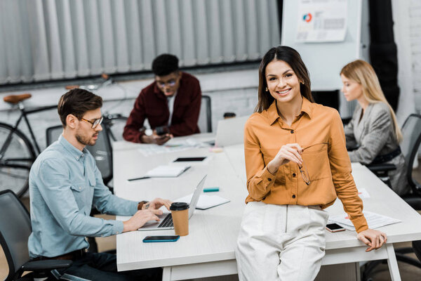 smiling businesswoman looking at camera with multiracial colleagues behind in office