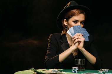 çekici kız ceket ve yüz poker kartları ile kapsayan ve kamera Casino bakarak şapka