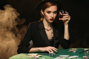 çekici kız ceket ve casino ve kameraya arıyor poker masasında bardak viski holding şapkası
