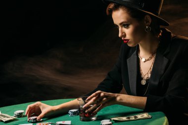 çekici kadın ceket ve casino poker masasında bardak viski tutan şapka yan görünüm