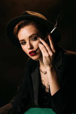 çekici kız ceket ve şapka siyah izole ve kameraya bakarak masada Sigara İçilmeyen