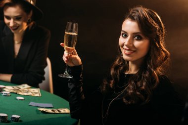 çekici kız holding bardak şampanya casino ve kameraya arıyor poker masasında gülümseyen