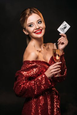 uzak seyir çekici kız holding joker kartı ve şampanya siyah, izole kırmızı parlak elbiseli gülümseyen