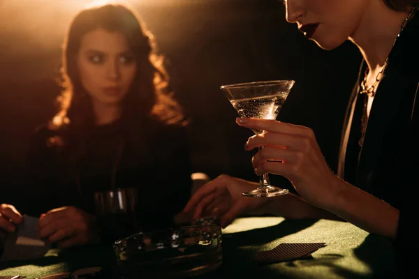 カジノ カクテルのガラスを保持している女性でのテーブルでポーカーをプレイする魅力的な女の子のトリミングされた画像  — 無料ストックフォト