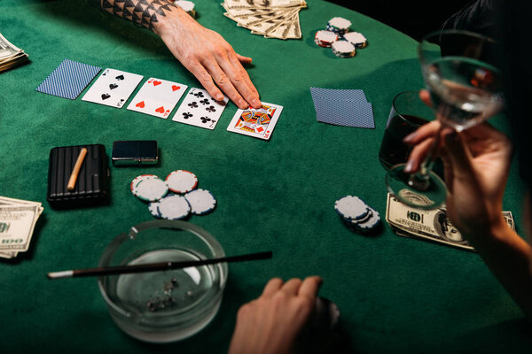 обрезанный образ женщины с татуированным мужчиной за покерным столом в казино, девушка с коктейлем в руках
